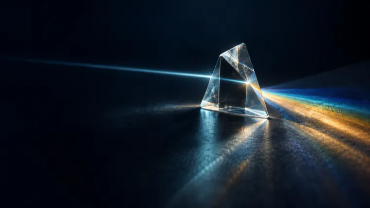 A glass prism splitting a narrow beam of light into separate colours on a dark surface.